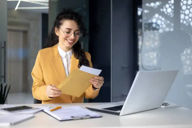 Photo of Successful hispanic woman inside office at work businesswoman received postal envelope letter notification with good news, female worker celebrating victory and good results achievement at workplace