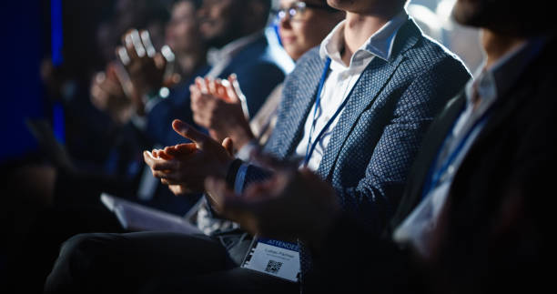 cierre de las manos de una multitud de personas aplaudiendo en la oscura sala de conferencias durante una presentación motivacional magistral. sala auditorio cumbre de tecnología empresarial llena de delegados. - ovacionar fotografías e imágenes de stock