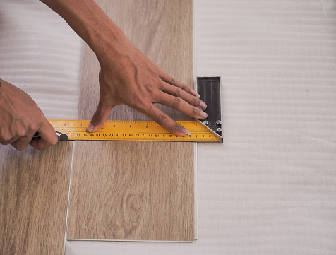 A technician is cutting luxury vinyl floor tiles with a cutter to lay the floor before placing it on the leveling foam.