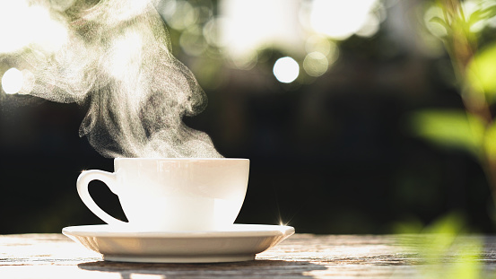 Coffee Cup, Mug. Close-up natural steam smoke of coffee from hot coffee cup on old wooden table in morning warm sunshine flare, outdoor view background. Concept hot drink, espresso, breakfast
