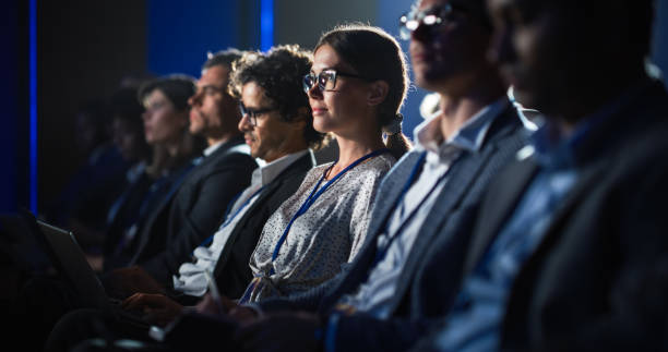 istock Female Sitting in a Dark Crowded Auditorium at a Tech Conference. Young Woman Using Laptop Computer. Specialist Watching Innovative Technology Presentation About New Software and High Tech Products. 1482844948