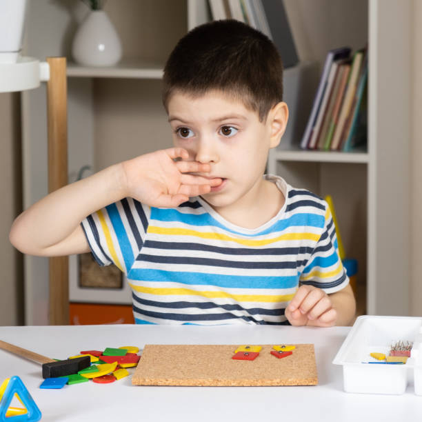 istock A 5-year-old boy bites his nails while sitting at a table and playing with mosaics in a children's room. Bad habits in children 1482844971