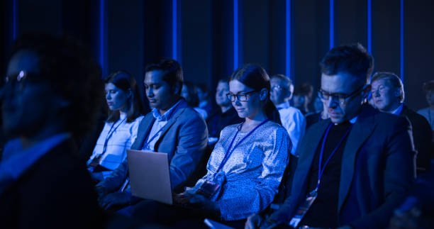istock Female Sitting in a Dark Crowded Auditorium at a Tech Conference. Young Woman Using Laptop Computer. Specialist Watching Innovative Technology Presentation About New Software and High Tech Products. 1482845024