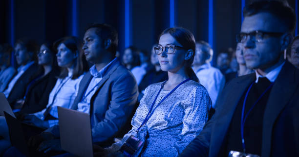 istock Male Sitting in a Dark Crowded Auditorium at a Tech Conference. Professional Using Laptop Computer. Specialist Watching Innovative Technology Presentation About New Software and High Tech Solutions. 1482845438