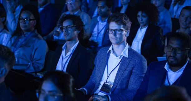 istock Male Sitting in a Dark Crowded Auditorium at an International Conference. Professional Using Laptop Computer. Innovative Presentation Concept: Technology, Science, Health, Mindfulness, Business. 1482845614