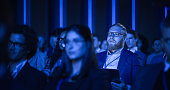 Portrait of a Handsome Man Sitting in a Dark Crowded Auditorium at a Tech Conference. Young Man Focused on Keynote Presentation. Specialist Inspired by Latest Technology Advances.