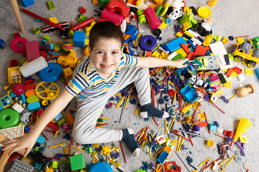 A little boy sits among scattered toys and smiles looking into the camera.
