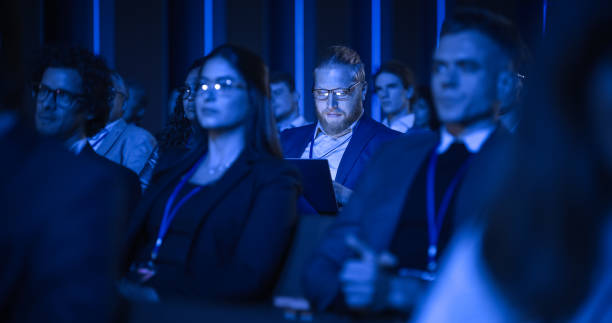 istock Young Bearded Man Attending an IT Conference in Crowded Audience. Delegate Using Laptop Computer. Happy Software Developer Watching Presentation About New High Tech Products and Data Protection. 1482845959