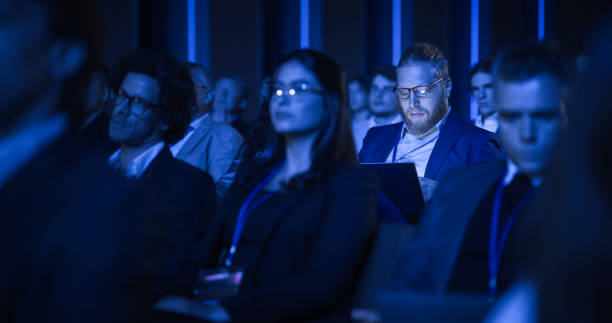 istock Young Bearded Man Attending an IT Conference in Crowded Audience. Delegate Using Laptop Computer. Happy Software Developer Watching Presentation About New High Tech Products and Data Protection. 1482846035