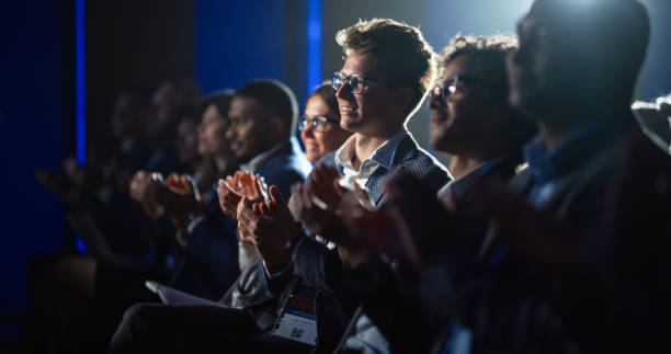 istock Young Male Sitting in a Crowded Audience at a Science Conference. Delegate Cheering and Applauding After an Inspirational Keynote Speech. Auditorium with Young Successful Specialist. 1482846413