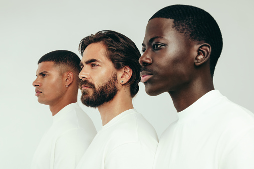 Three men with radiant and flawless skin standing side by side in a studio, looking confident in their healthy and glowing complexions. Diverse young men committing to a consistent skincare routine.