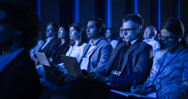 istock Young Man Sitting in a Crowded Audience at an IT Conference. Delegate Using Laptop Computer to Take Notes. Software Developer Watching Presentation About New High Tech Products and Cloud Solutions. 1482846755
