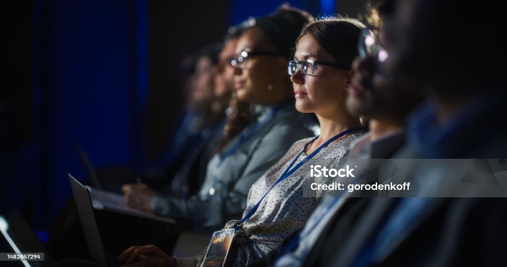 Young Psychologist Attending an International Cognitive Behavioral Therapy Seminar. Specialist Using Laptop Computer. Psychotherapy Professional Sitting in a Crowded Room on a Training Program. Conference - Event Stock Photo