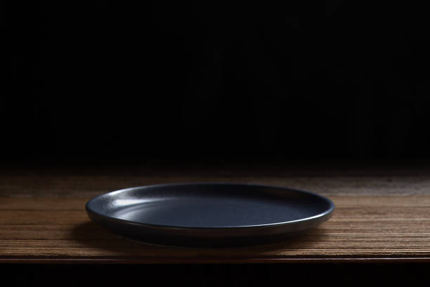 Ceramic navy blue plate on wooden board and black backdrop for presentation menu and montage food style.