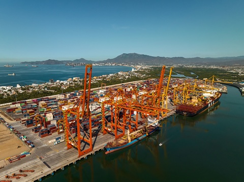 Manzanillo, Mexico – February 25, 2023: This aerial view of a bustling port features multiple large cranes and cargo ships, as well as an expansive coastline
