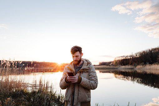 The man using the smartphone at the lake background at the sunset in spring