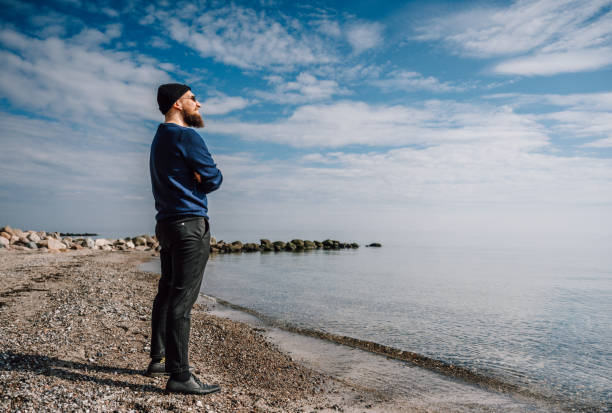 istock Cool young man with a beard, sunglasses and a cap is standing on the beach 1482858994