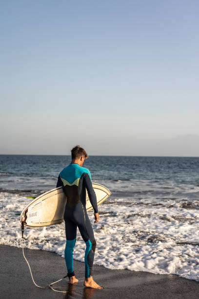 A surfer walks along a sandy beach and carries a surfboard in his hands