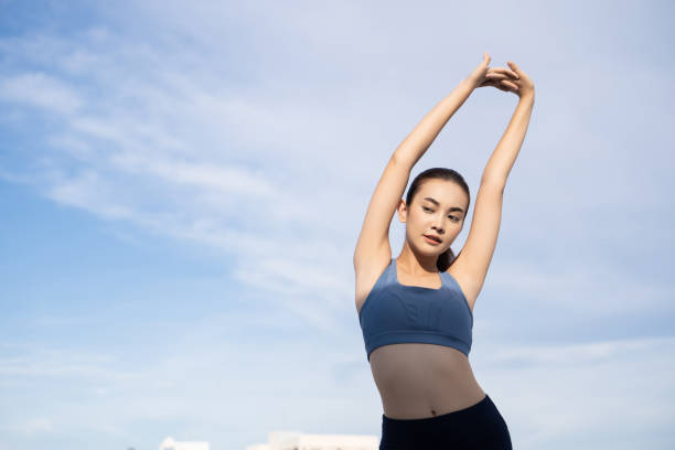 屋外の屋上でトレーニングを伸ばす若い美しいアジア人女性。彼女はウォーミングアップ - arm slim ストックフォトと画像
