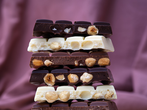 Stack of half chocolate bars with hazelnuts - milk chocolate, dark chocolate and white chocolate on burgundy background.