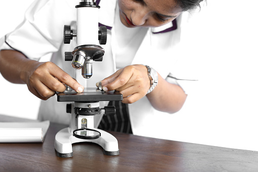 Young woman in formal wear observing slide using a microscope at laboratory.