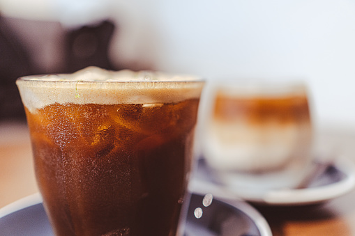 A glass of iced lemon americano with bokeh closeup and latte in the rear.