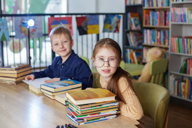 istock Schoolchildren reading books together while sitting at table in library. Back to school 1482865998