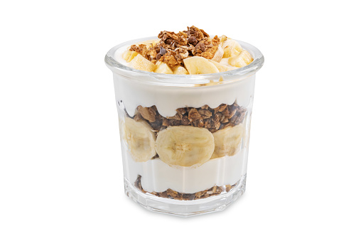 Banana Greek yogurt chocolate granola parfait in a glass on a white isolated background. toning. selective focus