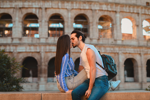 Romantic couple resting on ledge and kissing in front of Colosseum
