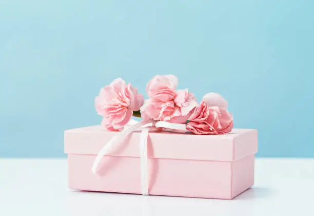 Pink gift box with tender pink carnation flowers. Blue background. Gift or holiday concept. Mothers Day, birthday wedding or St Valentines day with copy space. Minimal
