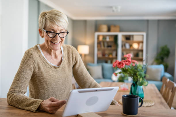 Senior woman caucasian female hold credit card online shopping at home One mature senior woman grandmother sit at home use credit or debit card for online shopping browse internet stores buying stuff use digital tablet real people copy space old woman smiling tablet stock pictures, royalty-free photos & images