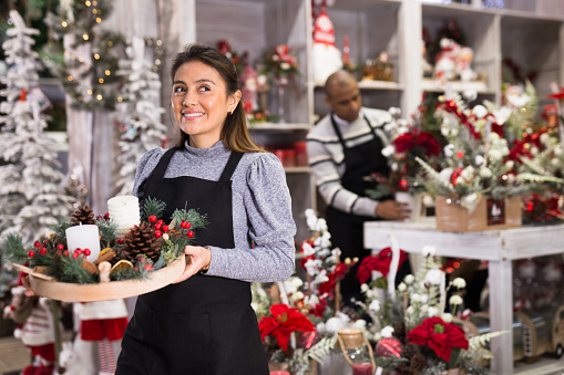 Positive owner of a flower shop prepares New Year decorations and arrangements