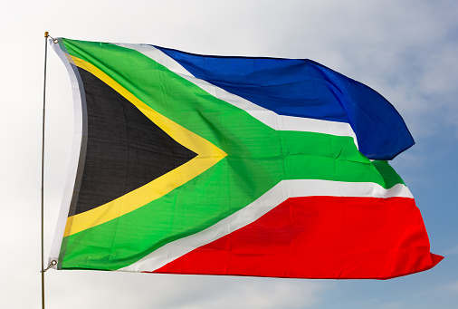 Against background of cloudy sky, cloth fabric flag of South Africa waves on flagpole.Isolated.Close up