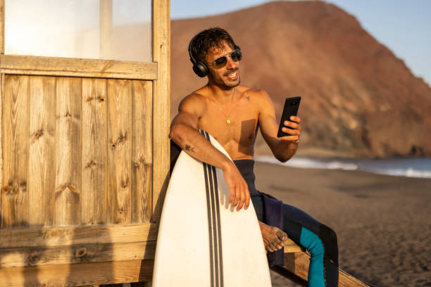 istock Surfer with a surfboard on the shore, sitting on an observation deck and taking a break from surfing the waves or waiting for a new opportunity to enjoy surfing 1482877931