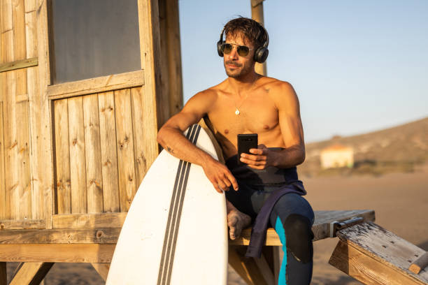 istock Surfer with a surfboard on the shore, sitting on an observation deck and taking a break from surfing the waves or waiting for a new opportunity to enjoy surfing 1482877942