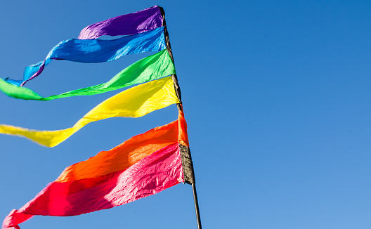 Colorful rainbow triangle flag shows up against the blue sky at the background.