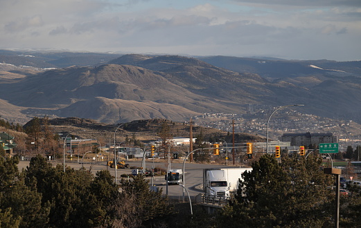 Kamloops, Canada - April 1, 2023: View from the hills of the Aberdeen neighbourhood in Kamloops near the Trans-Canada Highway. Traffic approaches the overpass. Background shows part of North Kamloops and the hill range of the Thompson-Nicola Regional District. Spring morning with light clouds.