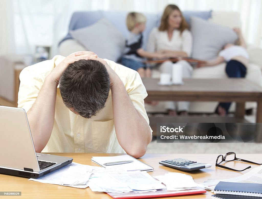 Man calculating his bills Man calculating his bills while his family are on the sofa Debt Stock Photo