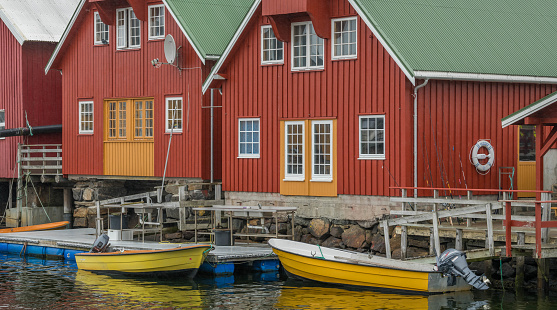 View on red traditional red painted rorbu green roofs and yellow vessels lying in the water. Norway.
