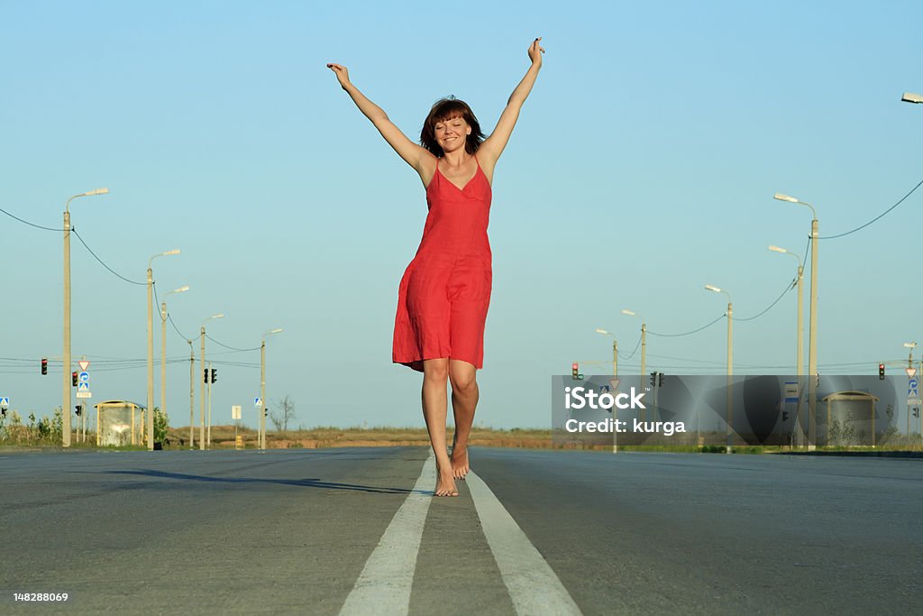 Fille en robe rouge Marchez pieds nus sur la route vide - Photo de Femmes libre de droits