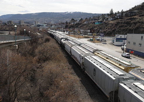 Kamloops, Canada - April 1, 2023: Freight trains wait near Riverside Park in the north end of downtown Kamloops. The West End neighbourhood includes hillside homes with views of the Thompson-Nicola Regional District. Spring morning with overcast skies.