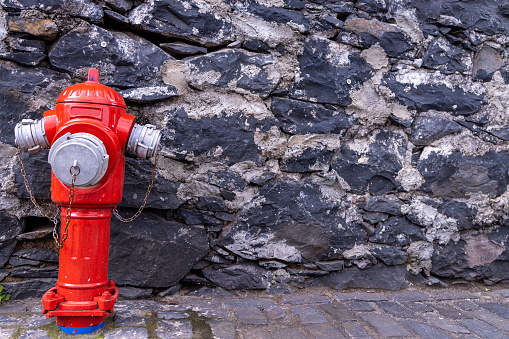 A red fire hydrant pipes used by fire fights to attach to their fire engines to pump water to put out fires on a brick wall located in the town of Funchal in Madeira Island in Portugal