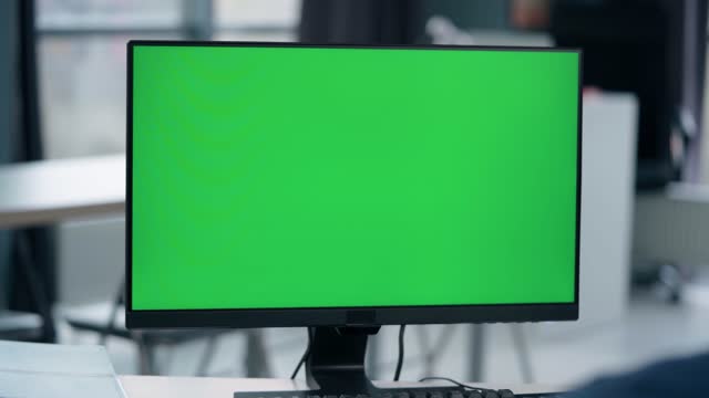Young Man Working At Computer With Green Mock Up Screen in Office