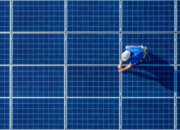 Solar panel installer installing solar panels with a big copy space Male engineer in blue suit and protective helmet installing photovoltaic panel system. Professional electrician mounting solar module on roof. Alternative energy ecological concept control panel stock pictures, royalty-free photos & images