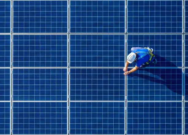 Male engineer in blue suit and protective helmet installing photovoltaic panel system. Professional electrician mounting solar module on roof. Alternative energy ecological concept