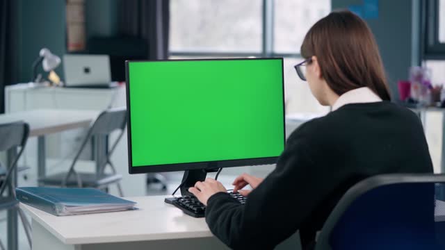 Woman Working At Computer With Green Mock Up Screen Sitting At Desk in Office