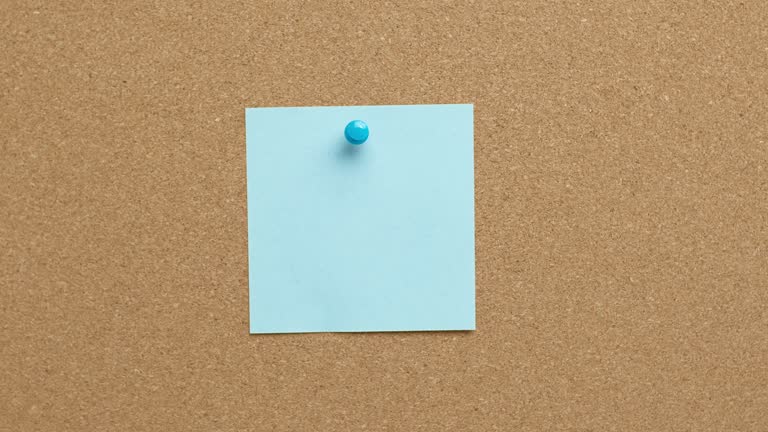 A woman's hand pins a blank paper note on a cork board. Post reminder. A place to write an idea.