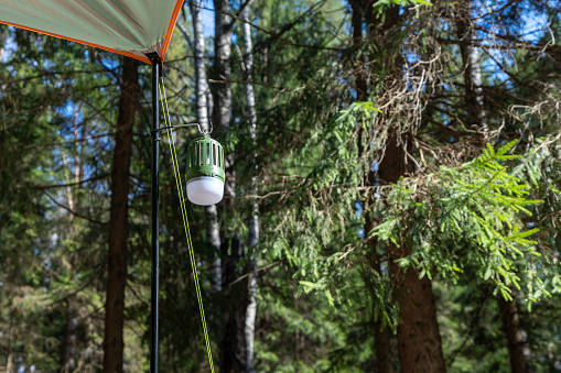 Close-up of a vintage design LED lantern hanging from the tent pole at an outdoor camping site.