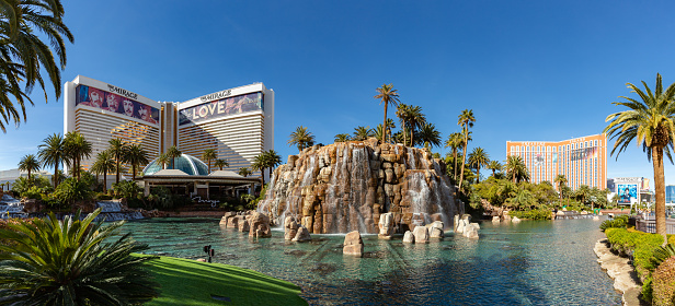 Las Vegas, United States - November 24, 2022: A picture of the Mirage Volcano and its surrounding pond and palm trees, with the main building on the left and the Treasure Island - TI Hotel and Casino, a Radisson Hotel on the right.