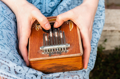 Crop anonymous female hands holding kalimba and playing music